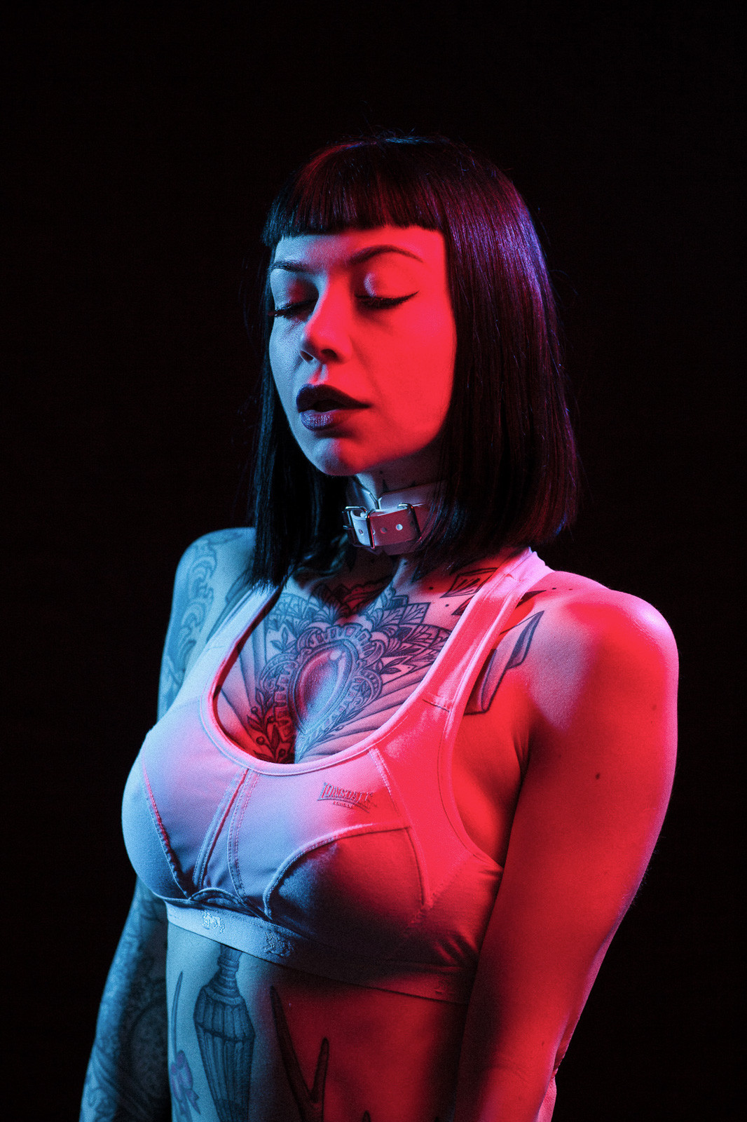 tattooed girl posing with white sportsbra in blue and red light studio light
