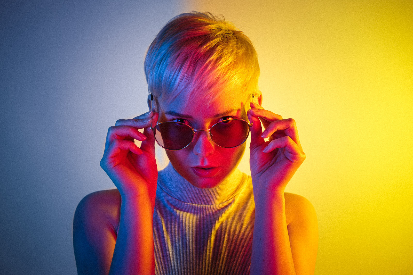 portrait of young woman with short hair wearing sunglasses with yellow and blue studio light
