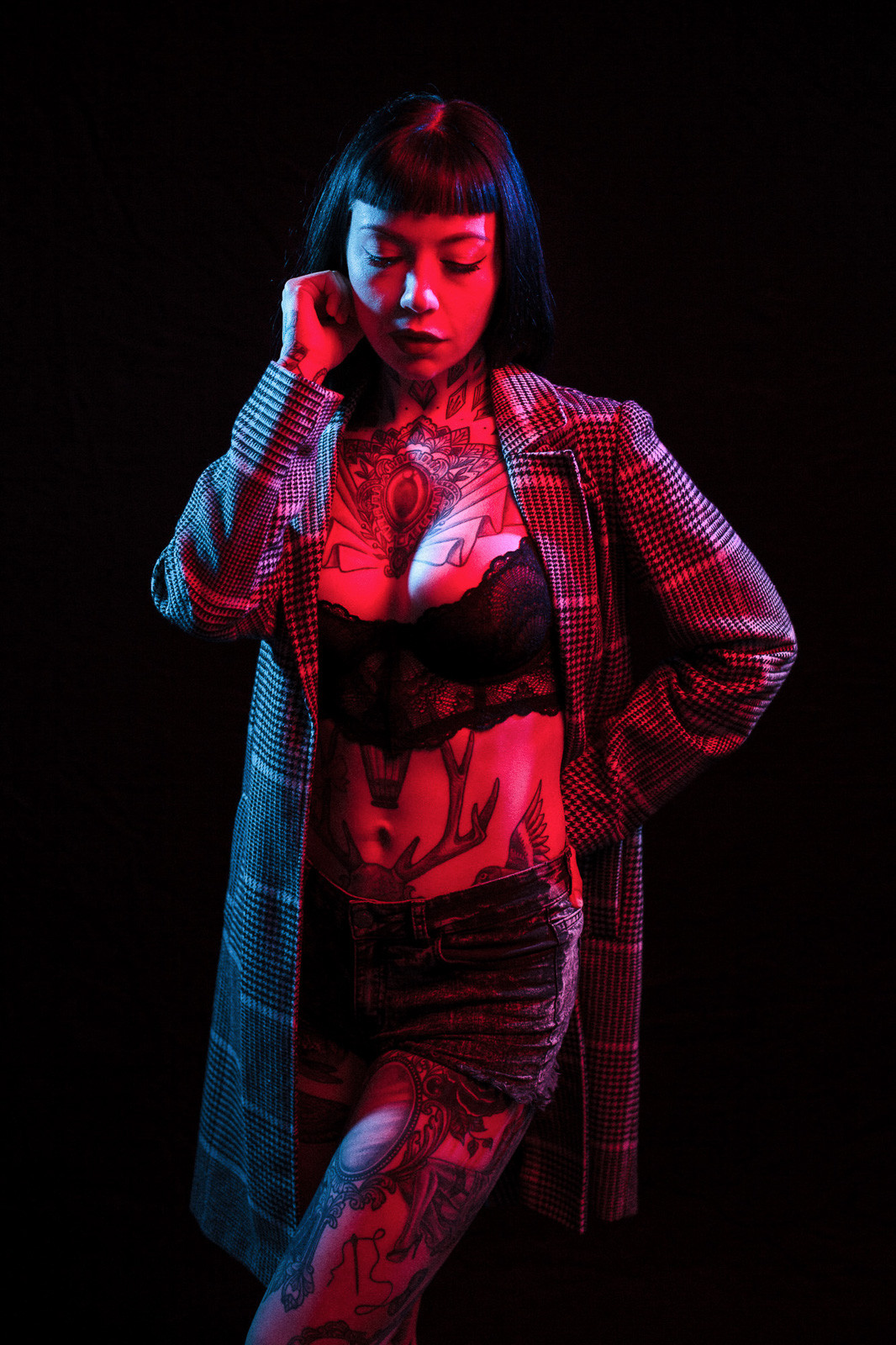 tattooed girl posing with overcoat in blue and red light studio light