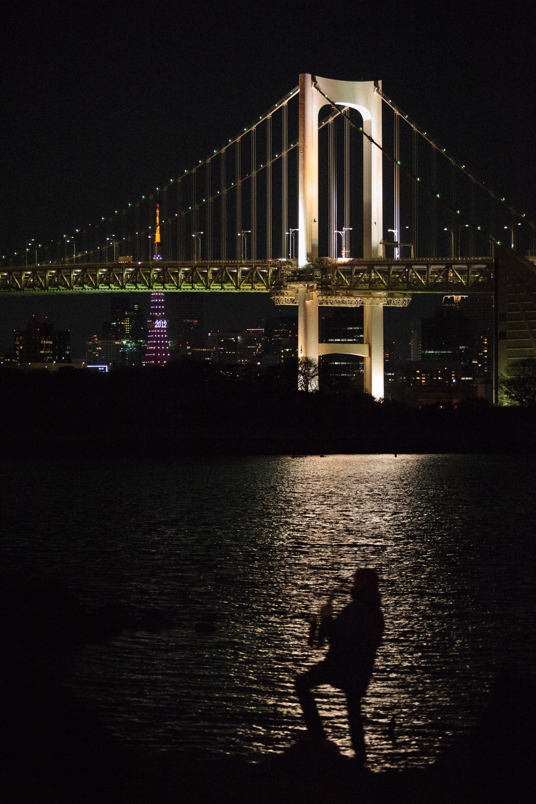saxophone player at night in tokyo in front of rainbow bridge